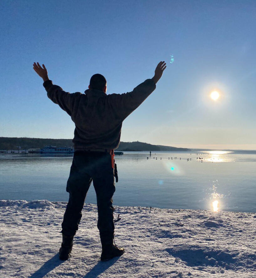 „Startbild –Willenstärke durch Herzenskräfte Energie und Freiheit in der Natur“ „Dennis Jahnke, Coach und energetischer Heiler, steht mit erhobenen Armen und gespreizten Beinen in X-Form am schneebedeckten Seeufer, Sonnenlicht spiegelt sich auf der Wasseroberfläche“