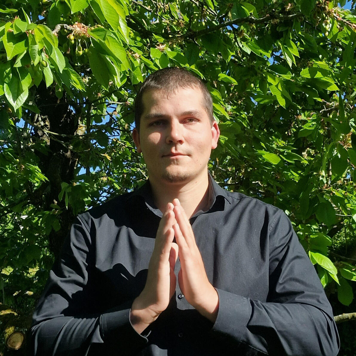 Dennis Jahnke Porträt „Porträt des Coaches und energetischen Heilers Dennis Jahnke vor einem Baum mit den Händen in Gebetsgeste“